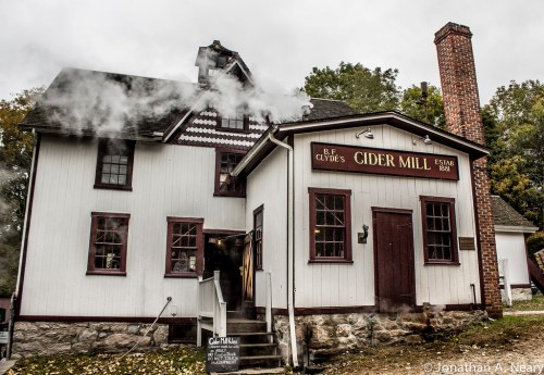 Historic cider mill building with smoke rising from the chimney, featuring a sign that reads "B & Clyde's Cider Mill."