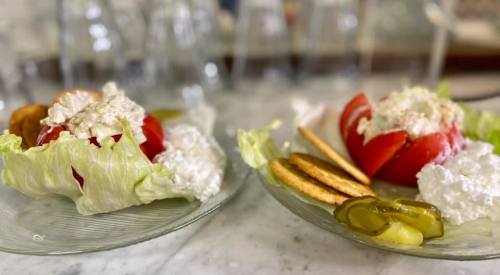 Two plates with lettuce, stuffed tomatoes, crackers, and pickles on a marble surface.