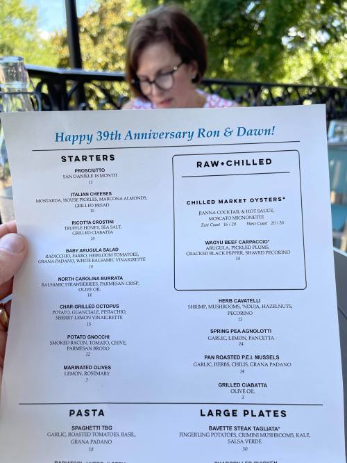 A menu for an anniversary dinner featuring starters, pasta, and large plates, with a woman in the background.