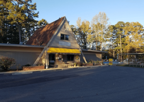 A triangular-roofed building with a yellow awning, surrounded by trees and a clear blue sky.