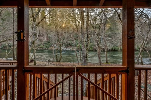 View of a serene river through a wooden porch, surrounded by trees and soft sunlight filtering through the branches.