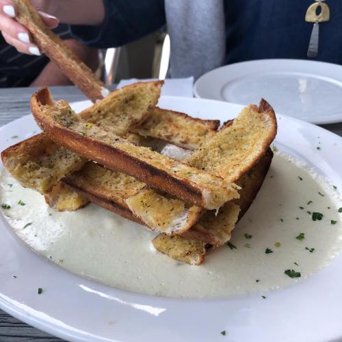 A stack of toasted bread on a plate, served with a creamy sauce and garnished with herbs.