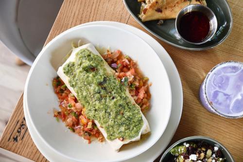 A plate featuring a burrito topped with green sauce, served on a bed of diced tomatoes and accompanied by sides.