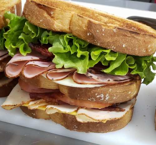 A stacked sandwich with layers of lettuce, ham, turkey, and bacon between toasted bread slices.