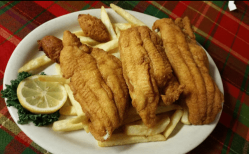 Plate of golden fried fish fillets served with French fries, a lemon slice, and a garnish of kale.