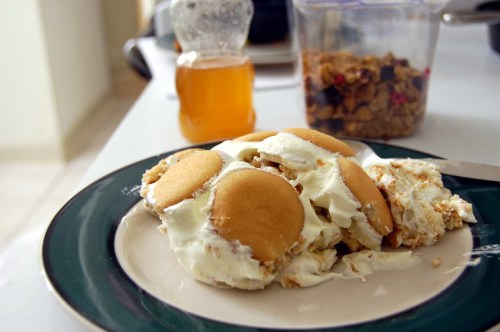 A plate of dessert featuring layered vanilla wafers and cream, with a jar of honey and a container of granola in the background.