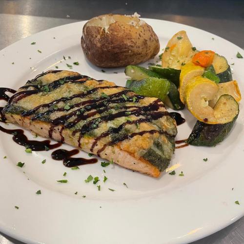 Grilled salmon with a balsamic glaze, served with sautéed vegetables and a baked potato on a white plate.