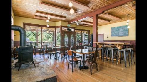 Cozy restaurant interior with wooden floors, tables, and a vintage stove, featuring large windows and warm lighting.