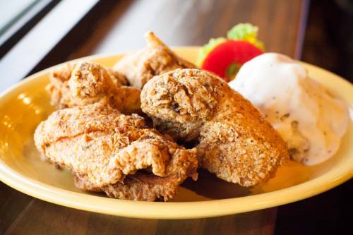 A plate of crispy fried chicken pieces served with a side of creamy coleslaw and a cherry tomato garnish.