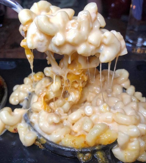 A close-up of creamy, cheesy macaroni and cheese with gooey, melted cheese stretching from a spoon.