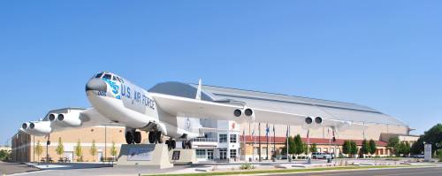A large aircraft displayed outside a modern building, with clear blue skies in the background.