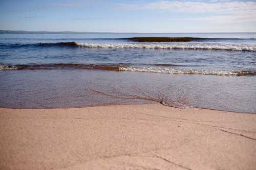 A serene beach scene with gentle waves lapping at the sandy shore under a clear blue sky.