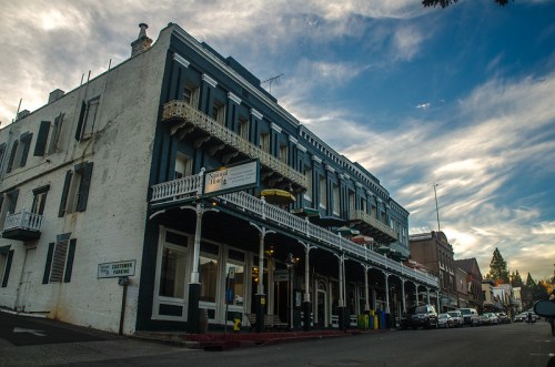 Historic building with balconies, under a blue sky with clouds, lined with parked cars on a street.