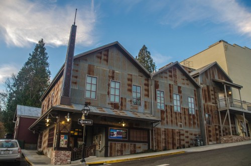 A rustic building with a metal exterior, featuring a tall sign and surrounded by trees under a blue sky.