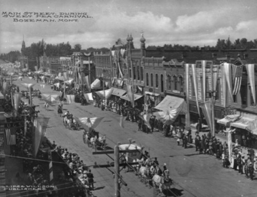 Historic black-and-white photo of Main Street during a carnival in Bozeman, Montana, with crowds and decorated buildings.