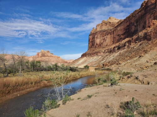 A serene landscape featuring a winding river, rocky cliffs, and blue skies with scattered clouds.