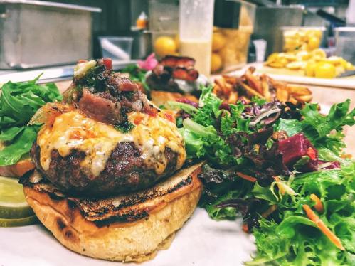 A gourmet burger topped with melted cheese and bacon, served with a side of mixed greens and fries.
