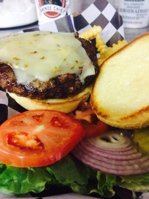 A juicy burger with melted cheese, lettuce, tomato, onion, and a side of crinkle-cut fries on a checkered plate.