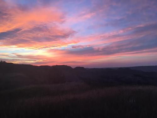 A vibrant sunset paints the sky in shades of pink and orange over rolling hills and valleys.