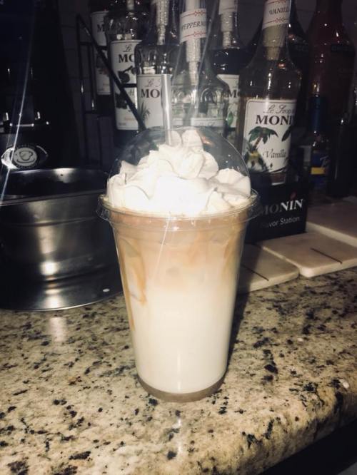 A creamy beverage in a clear cup topped with whipped cream and caramel drizzle, set on a granite countertop.