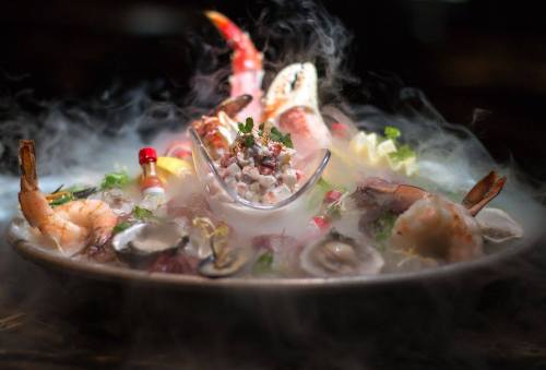 A seafood platter with shrimp, oysters, and a variety of garnishes, surrounded by mist for a dramatic effect.