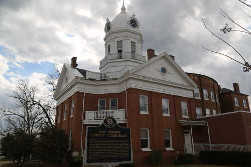 Historic Old Monroe County Courthouse with a clock tower, surrounded by cloudy skies and trees.