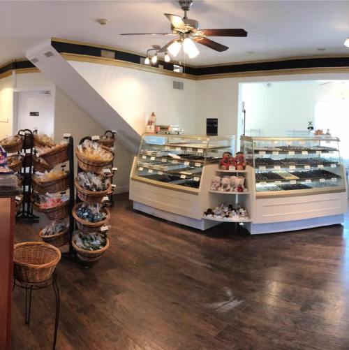 A cozy bakery interior featuring display cases of pastries and a staircase in the background. Warm lighting and wooden floors.
