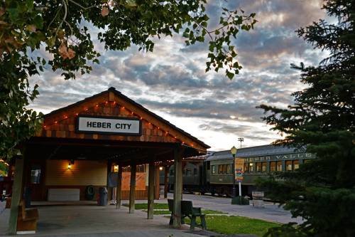 Heber City train station with a vintage train, surrounded by trees and a dramatic sky at sunset.