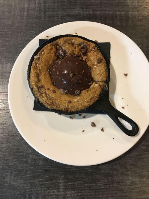 A warm chocolate chip cookie in a cast iron skillet, topped with a scoop of chocolate ice cream and chocolate bits.