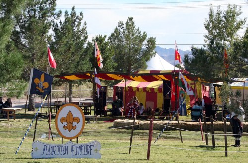 A colorful tent with flags in a grassy area, labeled "Adrian Empire," surrounded by trees and a clear blue sky.
