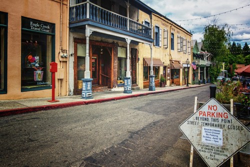 A quiet street lined with shops, featuring a "No Parking" sign and a street closure notice, under a cloudy sky.