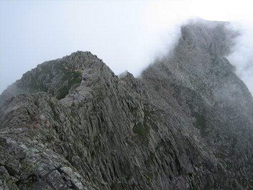 A rugged mountain ridge shrouded in mist, showcasing rocky terrain and steep cliffs.