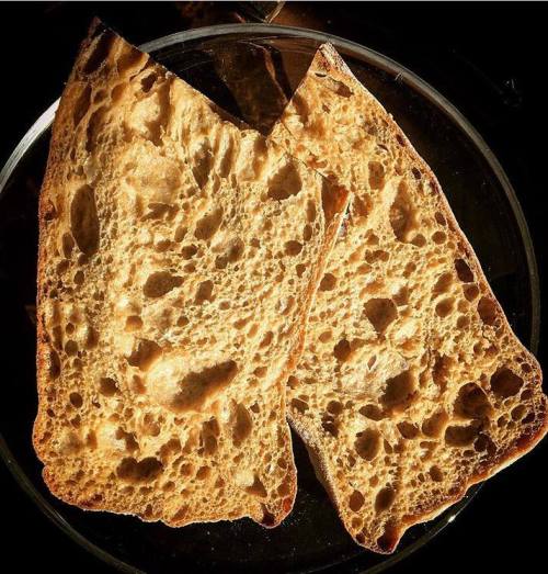 Two slices of toasted bread with a golden-brown crust and a porous, airy texture on a dark background.