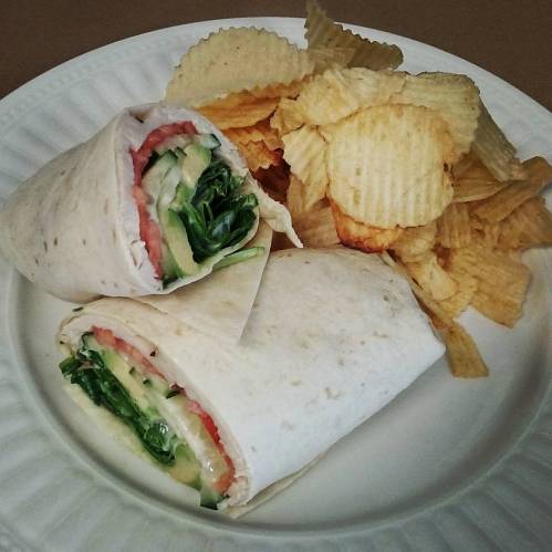 A plate with two wrapped sandwiches filled with lettuce and tomato, accompanied by a side of potato chips.
