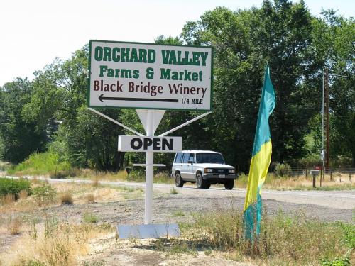 Sign for Orchard Valley Farms & Market and Black Bridge Winery, with an "Open" banner and a vehicle passing by.
