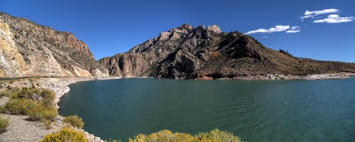 A panoramic view of a serene lake surrounded by rocky mountains and clear blue skies.
