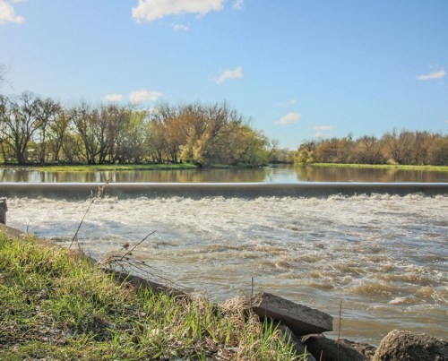 A serene river scene with flowing water, lush trees, and a clear blue sky.