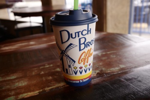 A Dutch Bros Coffee cup with a windmill design sits on a wooden table.