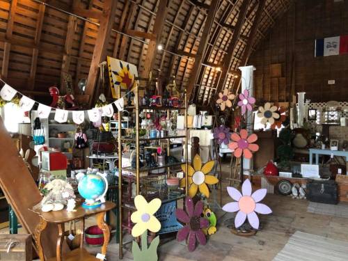 A cozy antique shop with wooden beams, colorful flower decorations, and various vintage items displayed throughout.