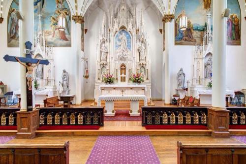 Interior of a church featuring an altar, ornate decorations, statues, and colorful paintings on the walls.