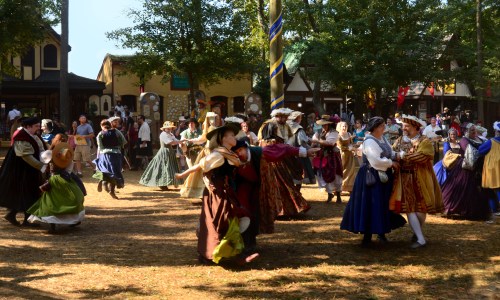 A lively scene of people in colorful Renaissance costumes dancing in a festive outdoor setting.