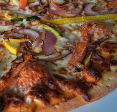 Close-up of a pizza topped with cheese, red onions, bell peppers, and various vegetables.