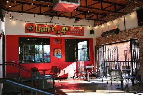 Interior of Lindy's on 4th, featuring red walls, string lights, and empty tables in a casual dining space.