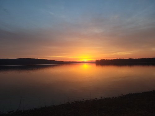A serene sunset over a calm lake, with vibrant orange and yellow hues reflecting on the water's surface.