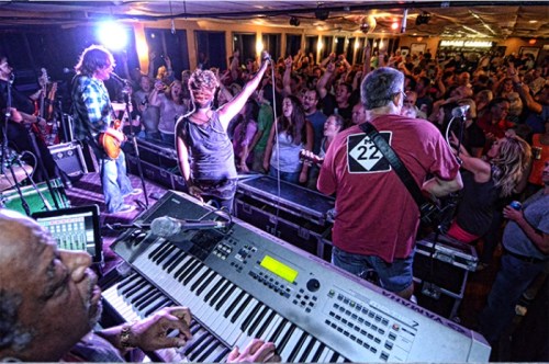 A lively band performs on stage while an enthusiastic crowd dances and enjoys the music.