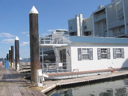 A houseboat docked at a marina, with wooden pilings and a blue sky in the background.