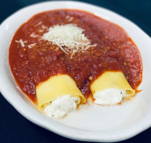 Plate of cannelloni filled with ricotta cheese, topped with marinara sauce and sprinkled with grated cheese.