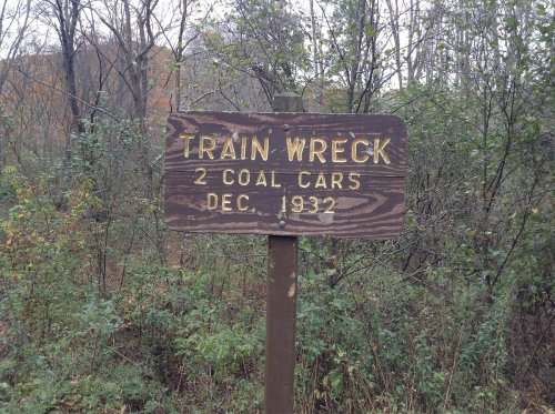 Sign marking the site of a train wreck with two coal cars, dated December 1932, surrounded by trees and foliage.