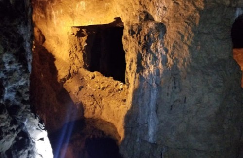 Dimly lit cave interior with rocky walls and an opening in the background, illuminated by soft orange light.