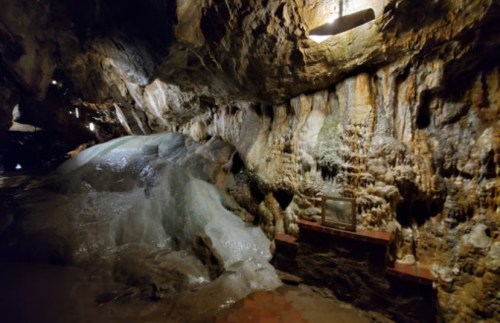 A dimly lit cave interior featuring rock formations and a frozen section of ice on the ground.